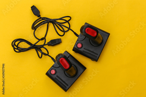Two wired retro joysticks with wound cable on yellow background. Video game, gaming. Top view