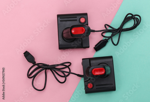 Two wired retro joysticks with wound cable on pink blue background. Video game, gaming. Top view