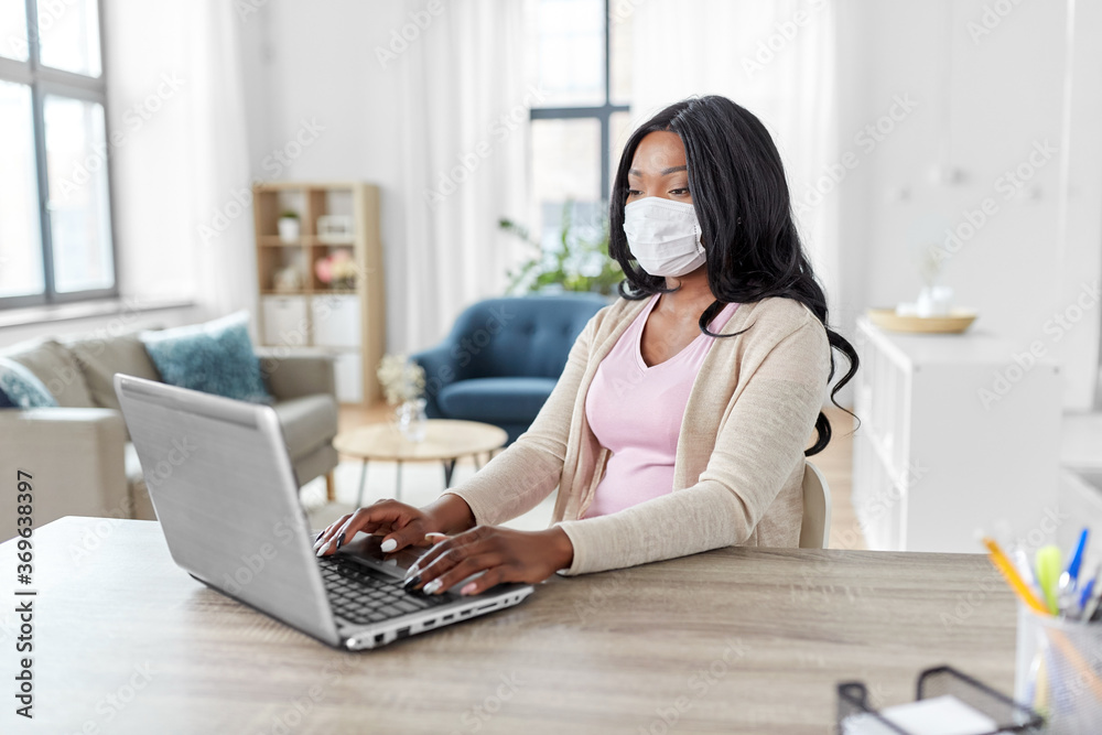 quarantine, remote job and pandemic concept - african american woman wearing face protective medical mask for protection from virus disease with laptop computer working at home office