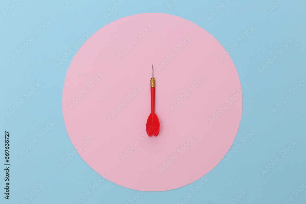 Red plastic dart with metal tip on blue pastel background with pink circle. Top view. Flat lay. Minimalism Red plastic dart with metal tip on blue pastel background with pink circle. Top view. Flat lay. Minimalism