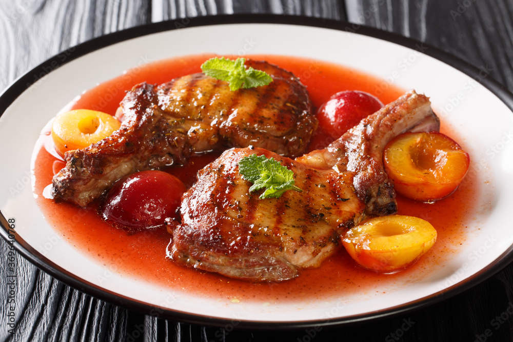 Fried spicy pork chop with fresh plums and fruit sauce close-up in a plate on the table. horizontal Fried spicy pork chop with fresh plums and fruit sauce close-up in a plate on the table. horizontal
