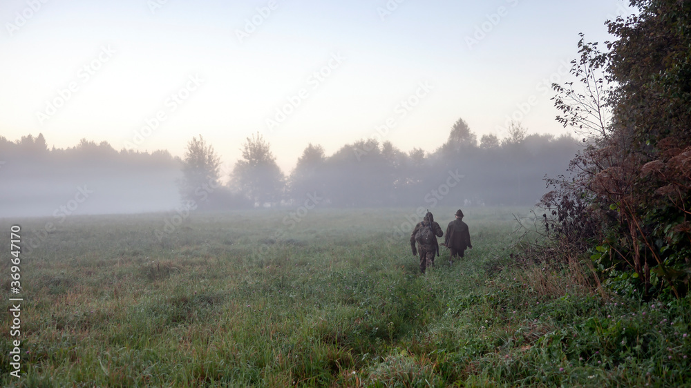 Hunters go in the morning in the fog along the edge of the forest