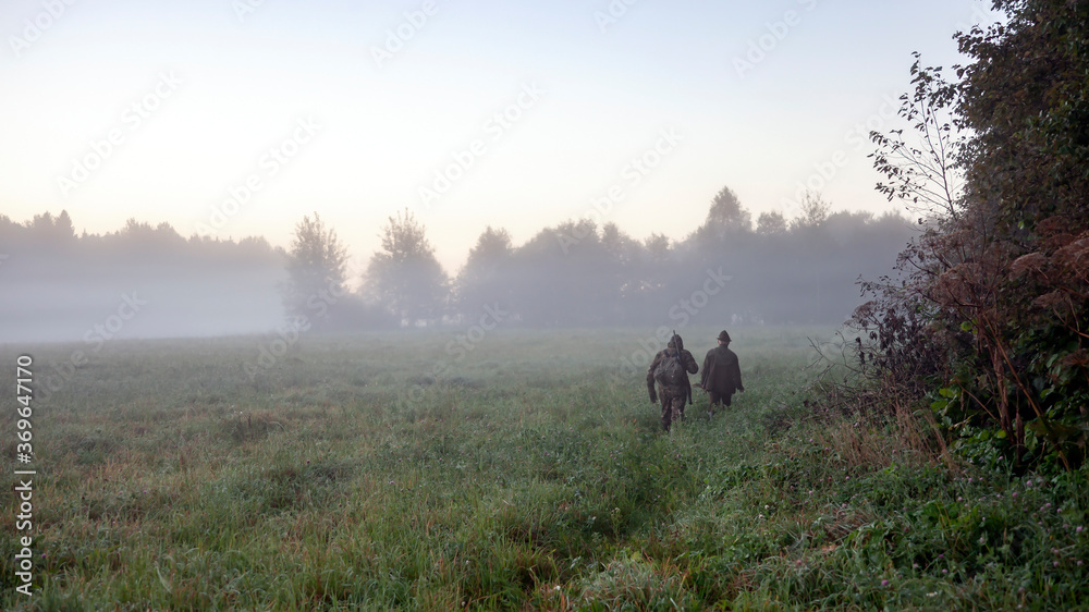 Hunters go in the morning in the fog along the edge of the forest Hunters go in the morning in the fog along the edge of the forest