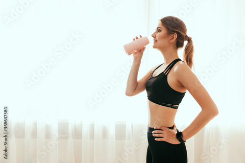 Fototapeta Naklejka Na Ścianę i Meble -  Woman in sportswear drinks water after training at home
