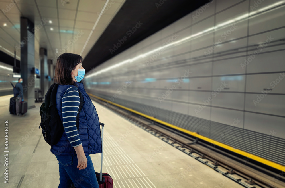 Mature woman travels in a protective mask. She is waiting for the train on an almost empty subway platform.