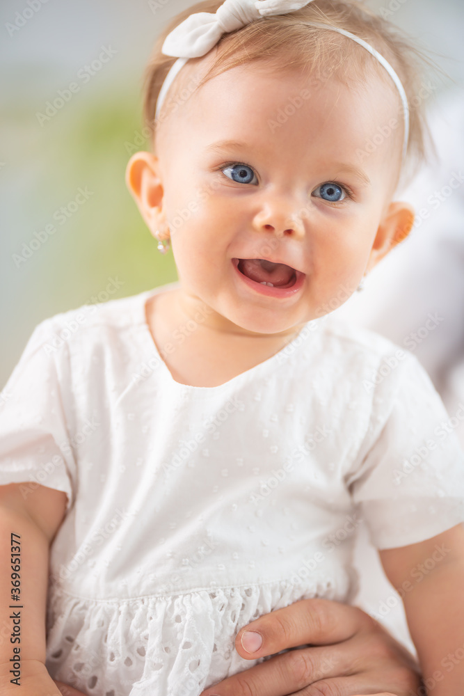 Happy infant child girl dressed in white laughing wearing headband and earrings