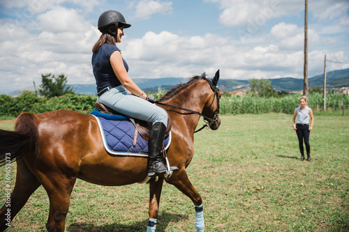 Beautiful young woman on a summer day rides with his horse and takes lessons from an experienced riding teacher - Millennial has fun with his animal friend