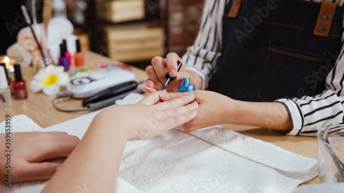 Manicure nail paint blue color in beauty salon. unrecognized manicurist woman in apron sitting at desk and working with customer hands. beautician applying color nail polish to client in studio
