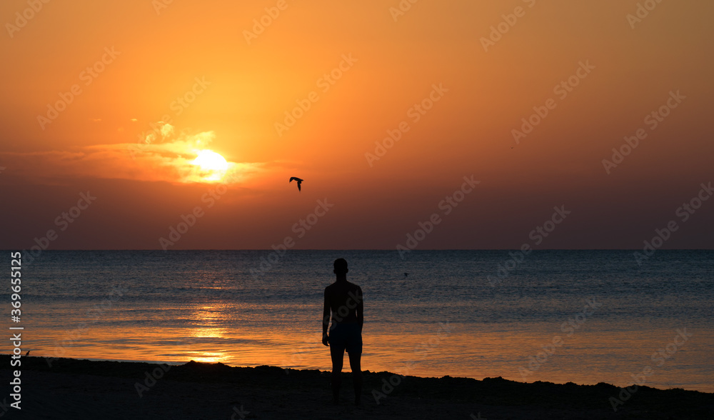 Sunrise by the sea. A man sits on the beach and admires the sunrise. Man silhouette