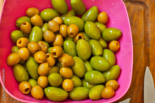 Yellow and green olives in a pink plate. Assorted olives close up.