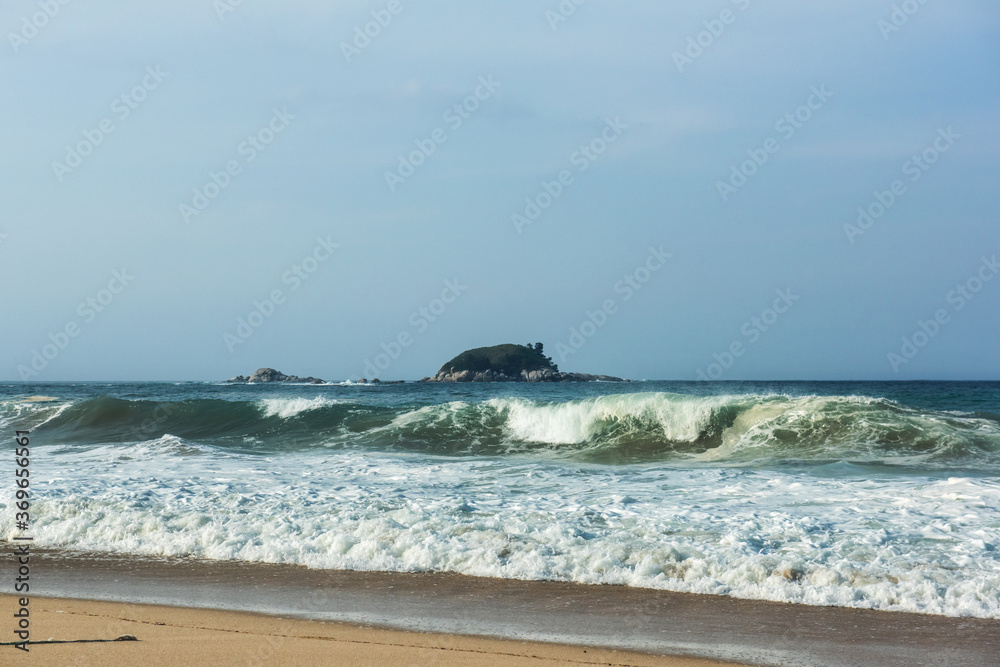 The huge waves crashing into ston island against the blue sky and horizon at summer sea shore.
