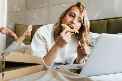Woman eating pizza and using laptop computer