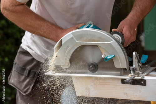 Hampshire, England, UK. 2020. Carpenter holding a circular saw to cut a plank of wood which creates a fine wood dust.