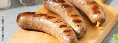 Fried sausages on a wooden serving Board on the light gray kitchen table. Fried sausages on a serving Board close-up. Banner