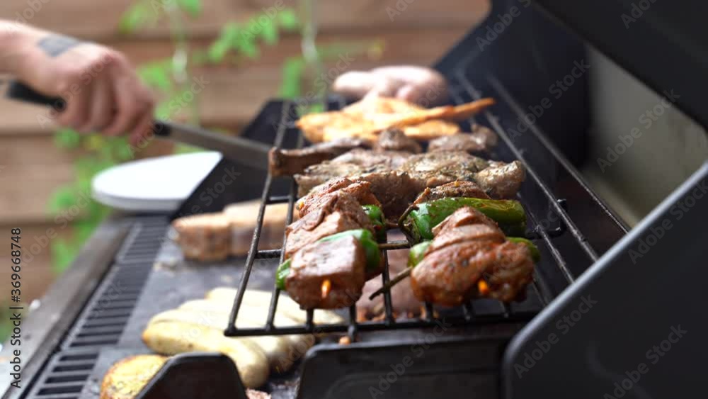 Close up shot of man using tongs to barbeque meat and sausages or bratwurst on a grill in backyard Close up shot of man using tongs to barbeque meat and sausages or bratwurst on a grill in backyard