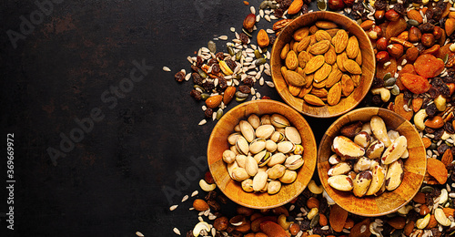 mix of different nuts and dried fruits in wooden bowl standing on rustic background