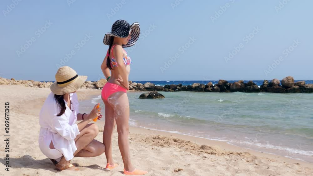 mom smears her daughter, 10-year-old girl, with sunscreen, on beach under hot sun, against sea background. Sun and UV protection. skin protection mom smears her daughter, 10-year-old girl, with sunscreen, on beach under hot sun, against sea background. Sun and UV protection. skin protection