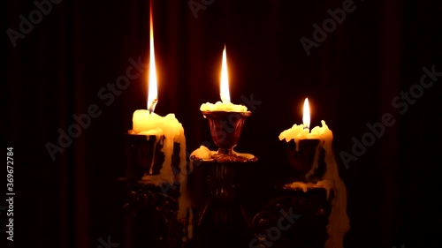 Three candles burn in a candlestick on a black background. Wind blowing on fire. Wax dripped from a burning candle.