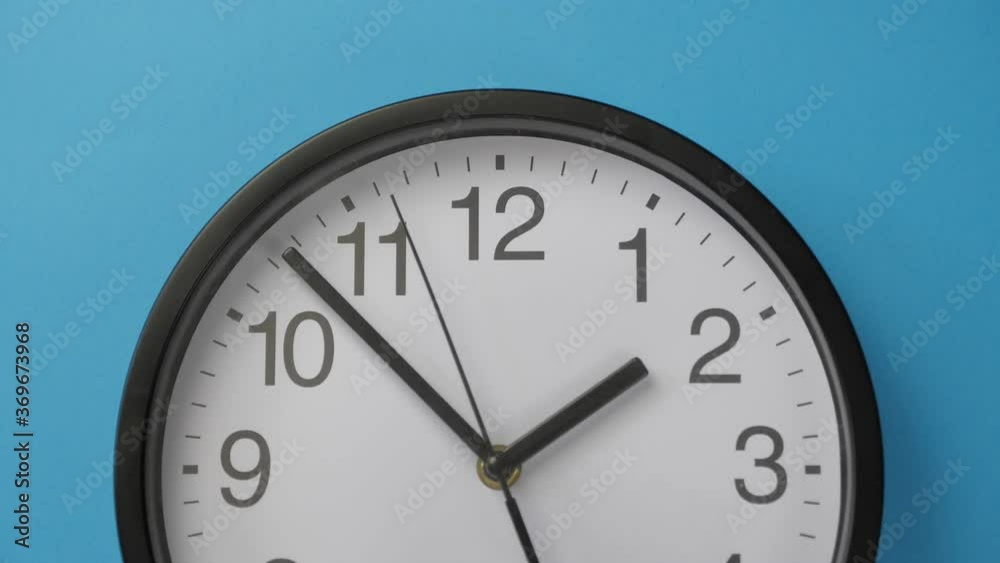 Close-up single white office clock hanging on a blue color wall. Close-up single white office clock hanging on a blue color wall.