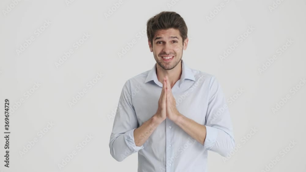 A charming man is asking for something while holding hands in a praying pose isolated over white background A charming man is asking for something while holding hands in a praying pose isolated over white background