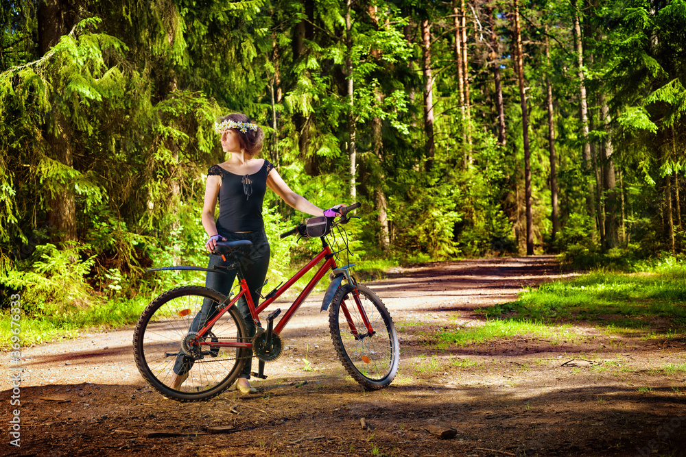 Woman in wreath of daisies with bike alone in the bright green forest