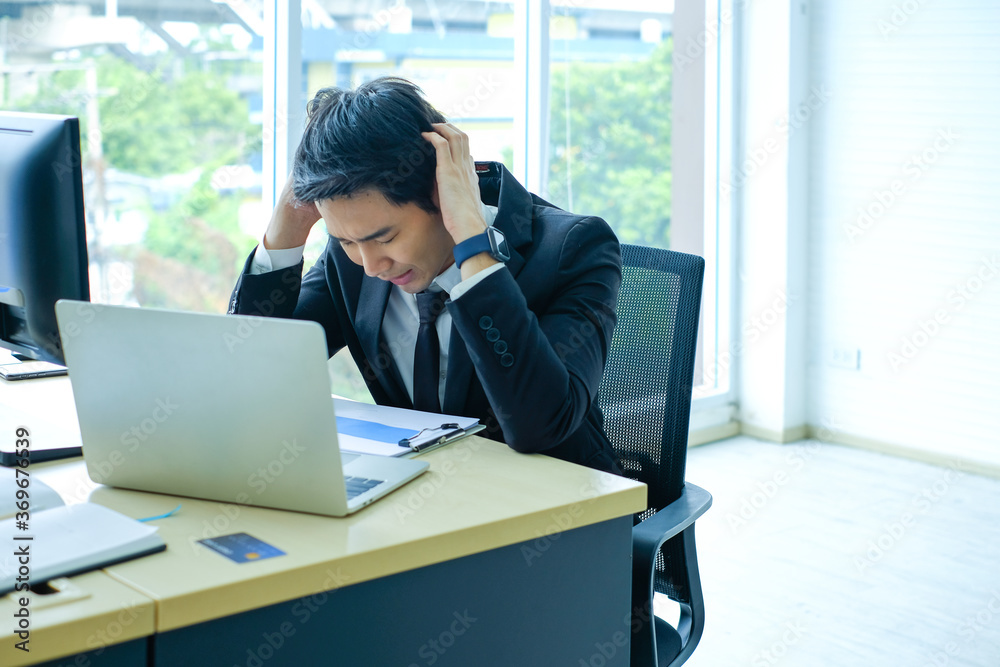 young Asian businessman in black suit sitting at the table looking a paper documents and thinking with headache at office. Asian man working hard and feeling Stressed young Asian businessman in black suit sitting at the table looking a paper documents and thinking with headache at office. Asian man working hard and feeling Stressed