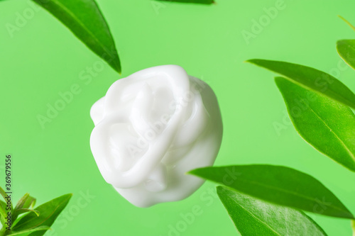 Fotografie Swirled silky white dollop of face cream body lotion on green background with fresh plants leaves