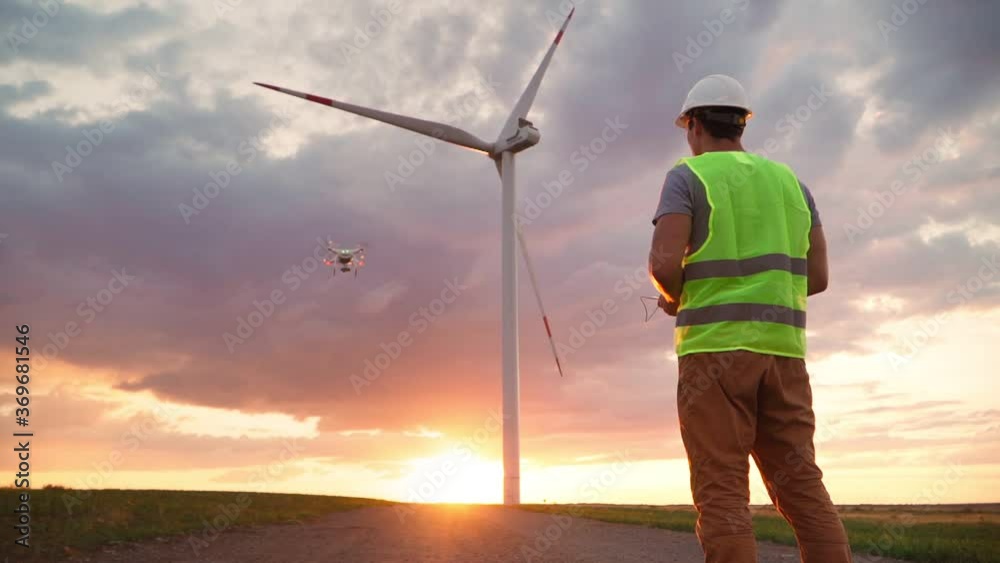 custom made wallpaper toronto digitalMan Professional Ecology Engineer in uniform and helmet holding remote controller for flying drone working at wind turbine on beautiful sunset background. Alternative to electrical energy