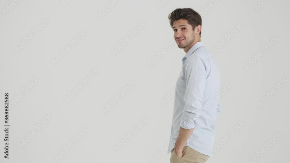 A smiling young man is walking from one side to another side and showing palm gesture to the camera isolated over white background A smiling young man is walking from one side to another side and showing palm gesture to the camera isolated over white background