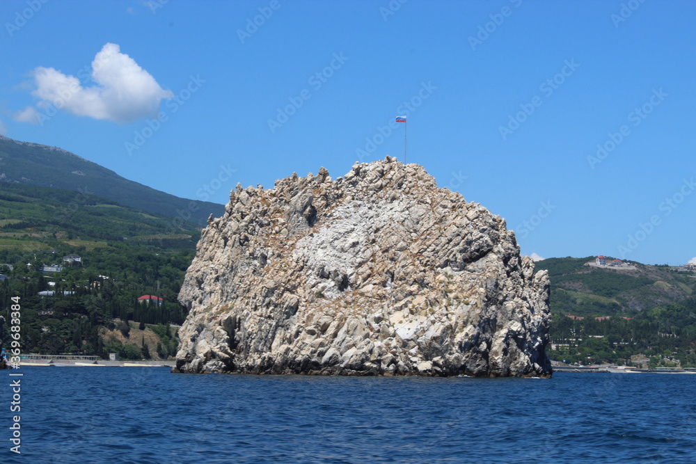 Seascape from the sea. A rocky coast that flows into the sea. Coast against the background of mountains and greenery. Clouds over the mountains Seascape from the sea. A rocky coast that flows into the sea. Coast against the background of mountains and greenery. Clouds over the mountains