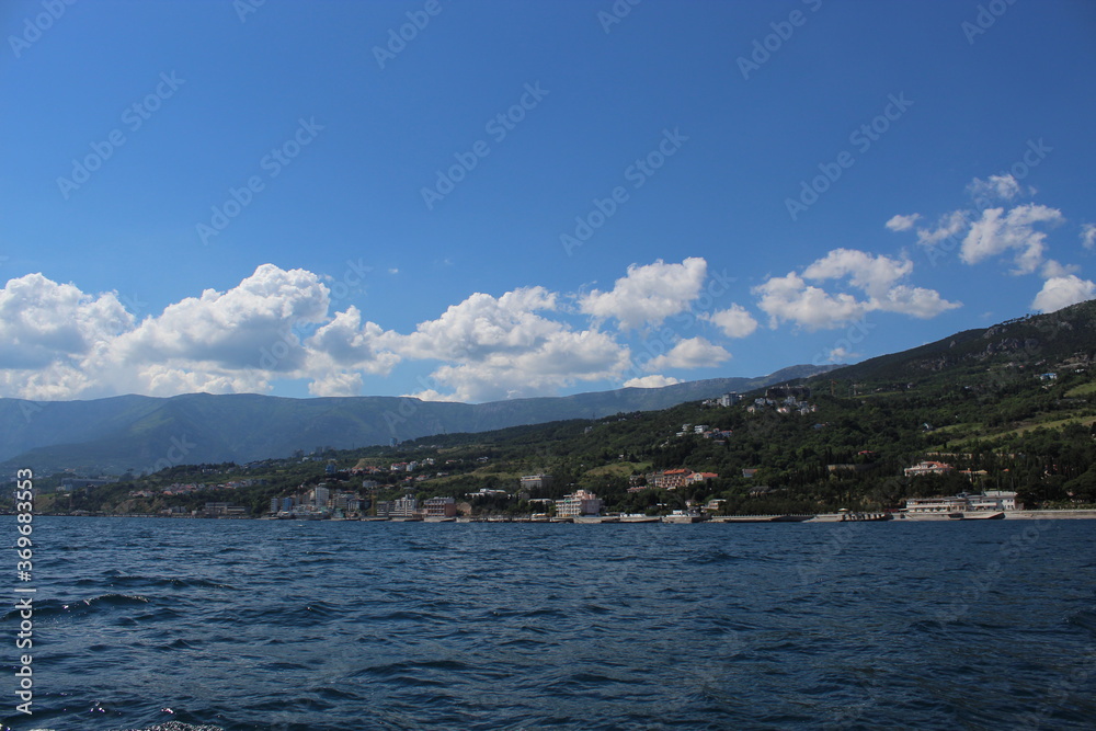 Seascape from the sea. A rocky coast that flows into the sea. Coast against the background of mountains and greenery. Clouds over the mountains