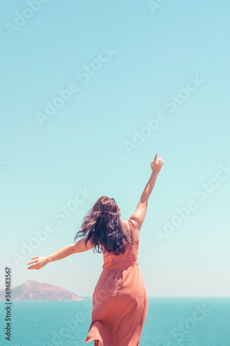 Young girl in dress looking at turquoise seascape and enjoying summer vacation