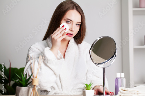 Smiling young woman washing her face with facial cleansing sponge at bathroom