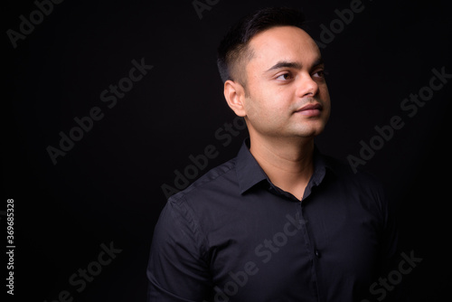 Portrait of young handsome Indian businessman against black background