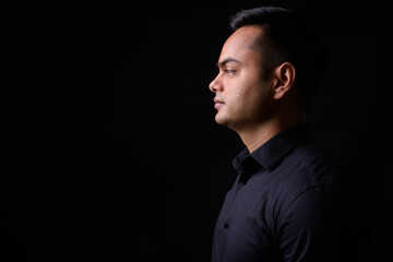 Portrait of young handsome Indian businessman against black background