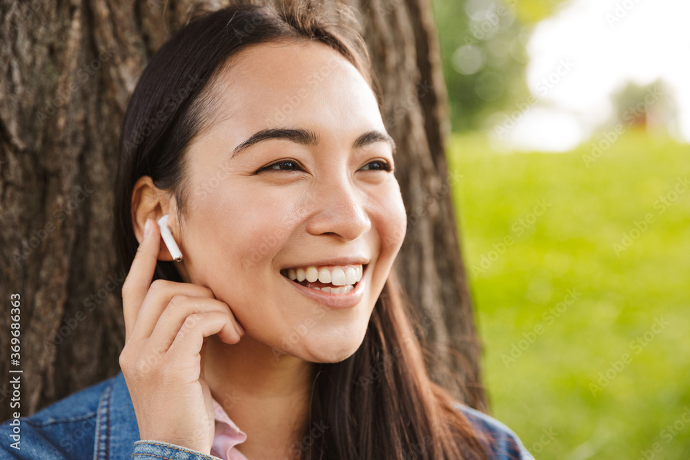Image of joyful asian student woman using wireless earphones and smiling Image of joyful asian student woman using wireless earphones and smiling