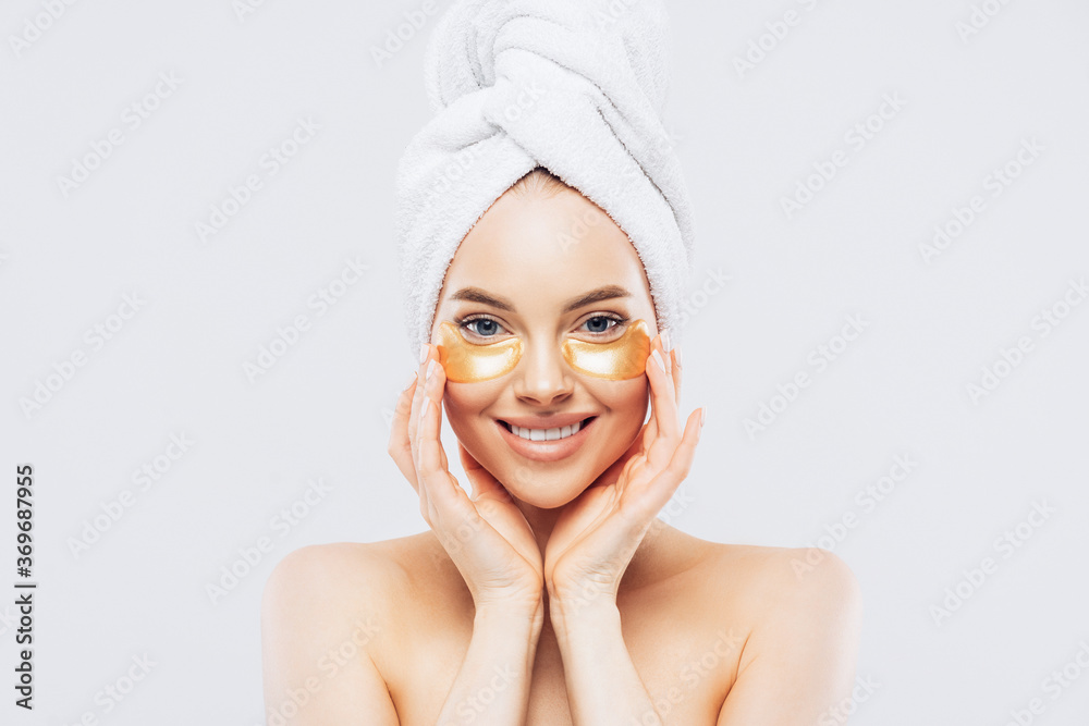Young pure beautiful gentle woman with a towel on head standing naked isolated looking camera take care of her skin with under eye patches. Young pure beautiful gentle woman with a towel on head standing naked isolated looking camera take care of her skin with under eye patches.