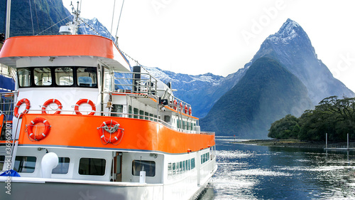 A local orange boat stop in the morning, with landscape of high mountain glacier in the background at Milford sound, New Zealand.