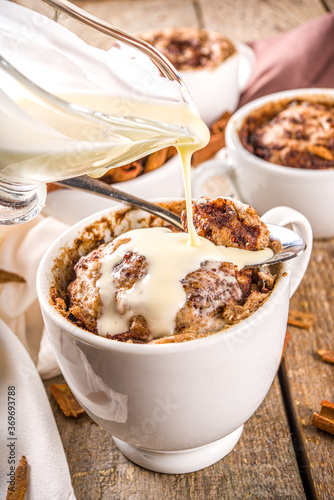 Cinnabon cake in mug. Fast simple microwave dessert idea, background for recipe. Cinnamon roll mugcake, with sugar and cream cheese topping, in different mugs, with cinnamon sticks on wooden backgroun