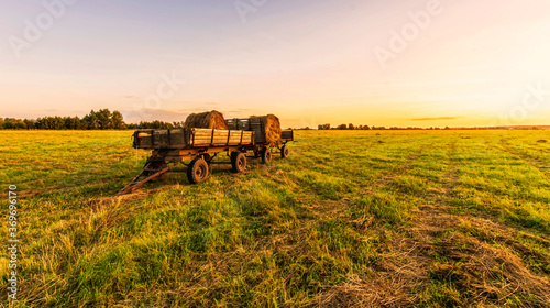 Old vintage carriage with hay stacks in green shiny field with beautiful sunset   hay cart in country valley during sunrise   wagon with haystacks and scenic view