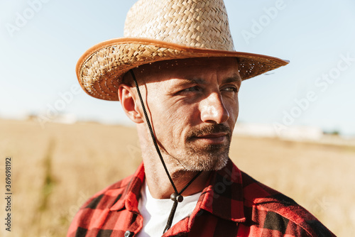 Image of unshaven adult man looking aside while standing at cereal field