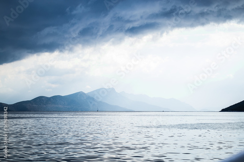 Dark clouds in the open sea. On the horizon are mountains on an island. Blue gradient.