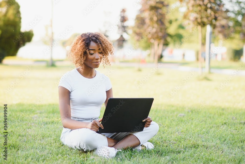Thoughtful cute mixed female international student with curly hair is sitting on fresh grass with modern laptop in public park, leaning on apple tree and wistfully looking aside during her break Thoughtful cute mixed female international student with curly hair is sitting on fresh grass with modern laptop in public park, leaning on apple tree and wistfully looking aside during her break