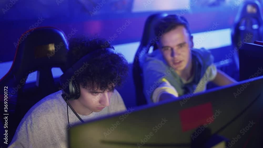 Young man giving advice to his friend but he is losing round of video game in modern cybersport club Young man giving advice to his friend but he is losing round of video game in modern cybersport club