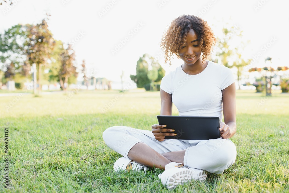 Cute black girl in a park. Lady in a white t-shirt and white jeans. Woman with tablet