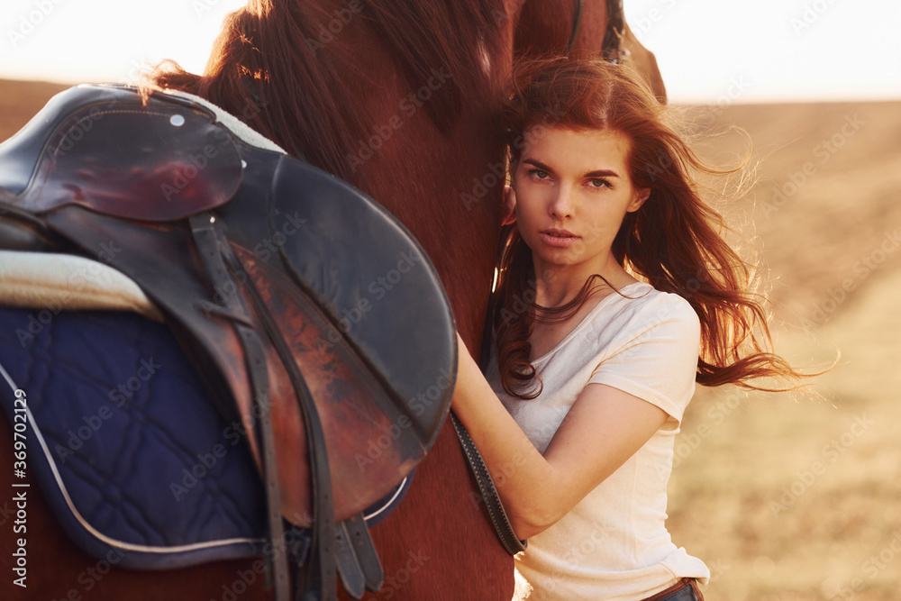 Young woman embracing her horse in agriculture field at sunny daytime