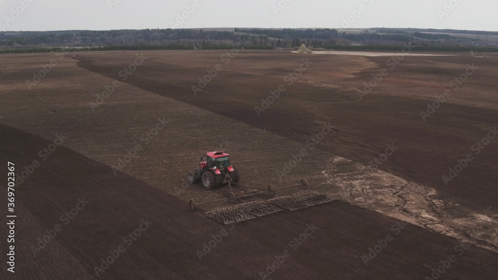 Aerial view tractor cuts furrows in farm field for sowing farm tractor with rotary harrow plow preparing land for sowing. Tractor with harrows prepares the agricultural land for planting crop