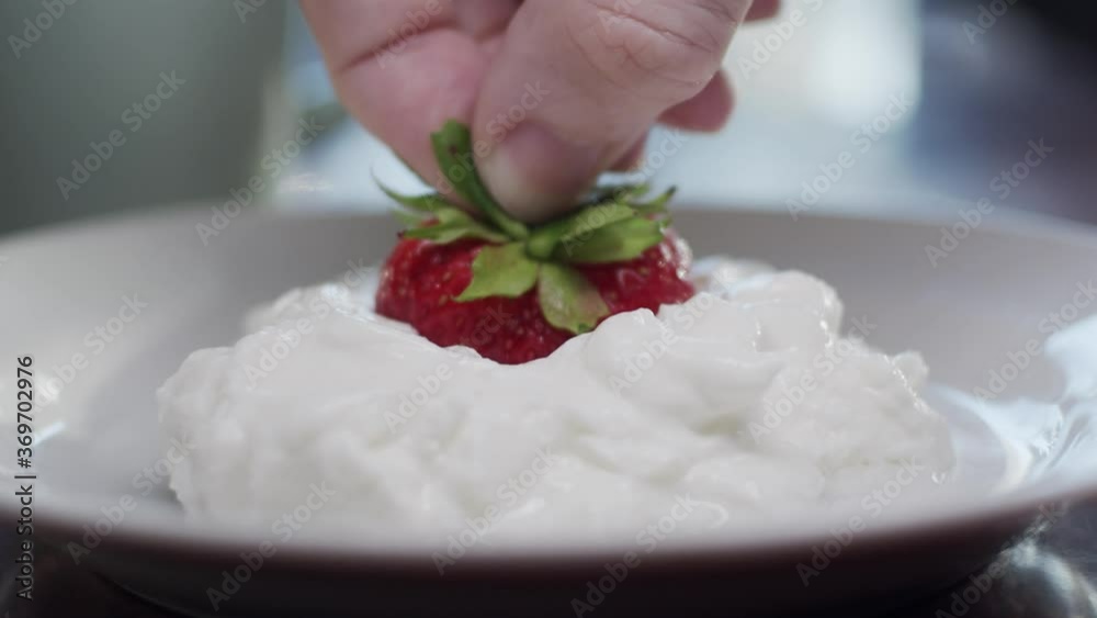 Strawberry in hand putting in cream on white plate, close up. Strawberry in hand putting in cream on white plate, close up.