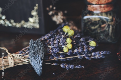 Black Kyanite crystal rock placed on dark brown wooden witch's table. Macro shot with blurred background, suitable as background for text. Bundle of dried lavender flower next to black Kyanite