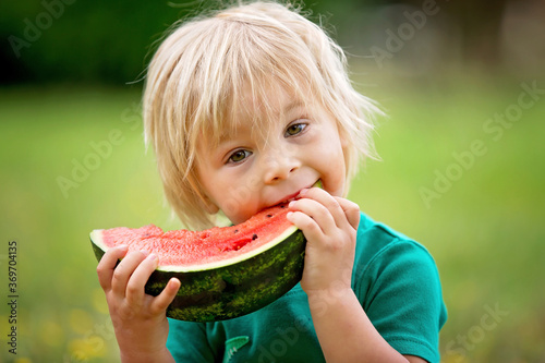 Cute little toddler child, blond boy, eating watermelon in the park